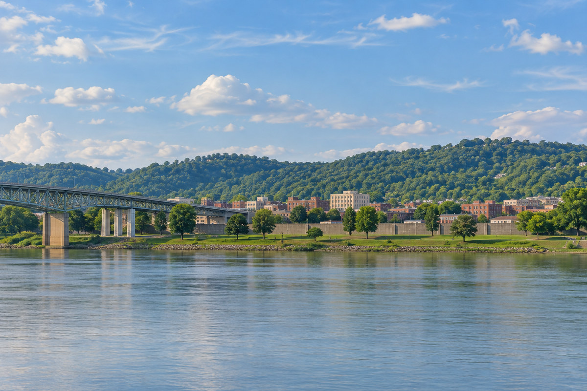 The Huntington riverfront along the Ohio River, a floodwall, a highway bridge and green hills beyond the river bottom